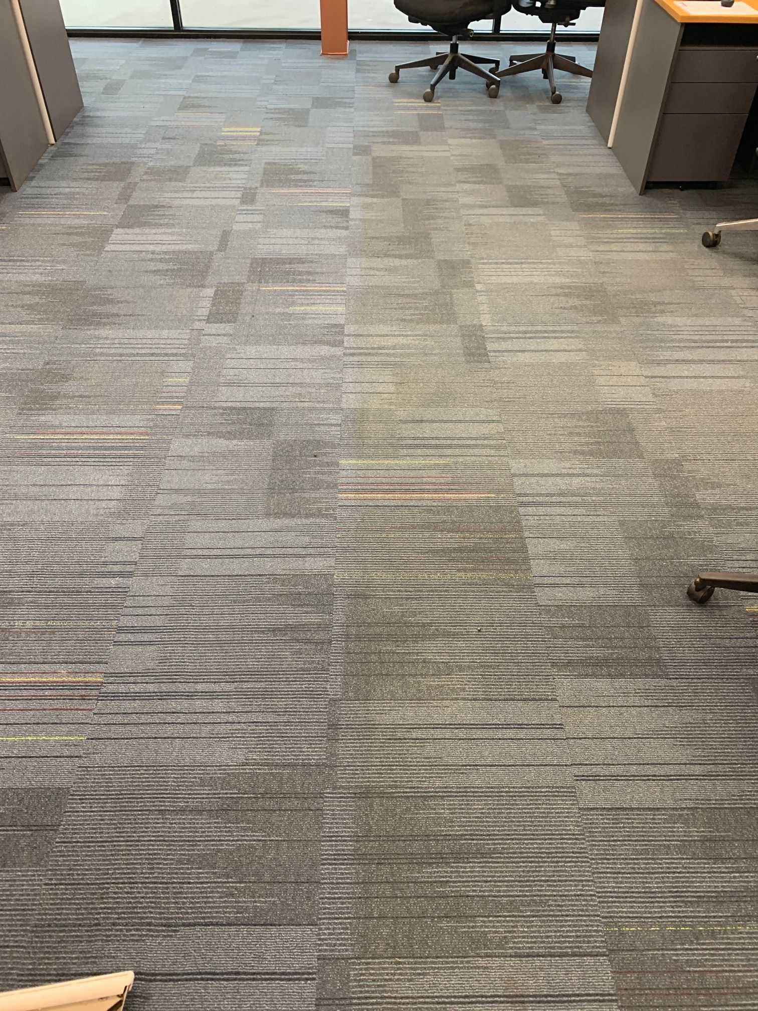 A gray carpeted floor in an office with a desk and chairs.