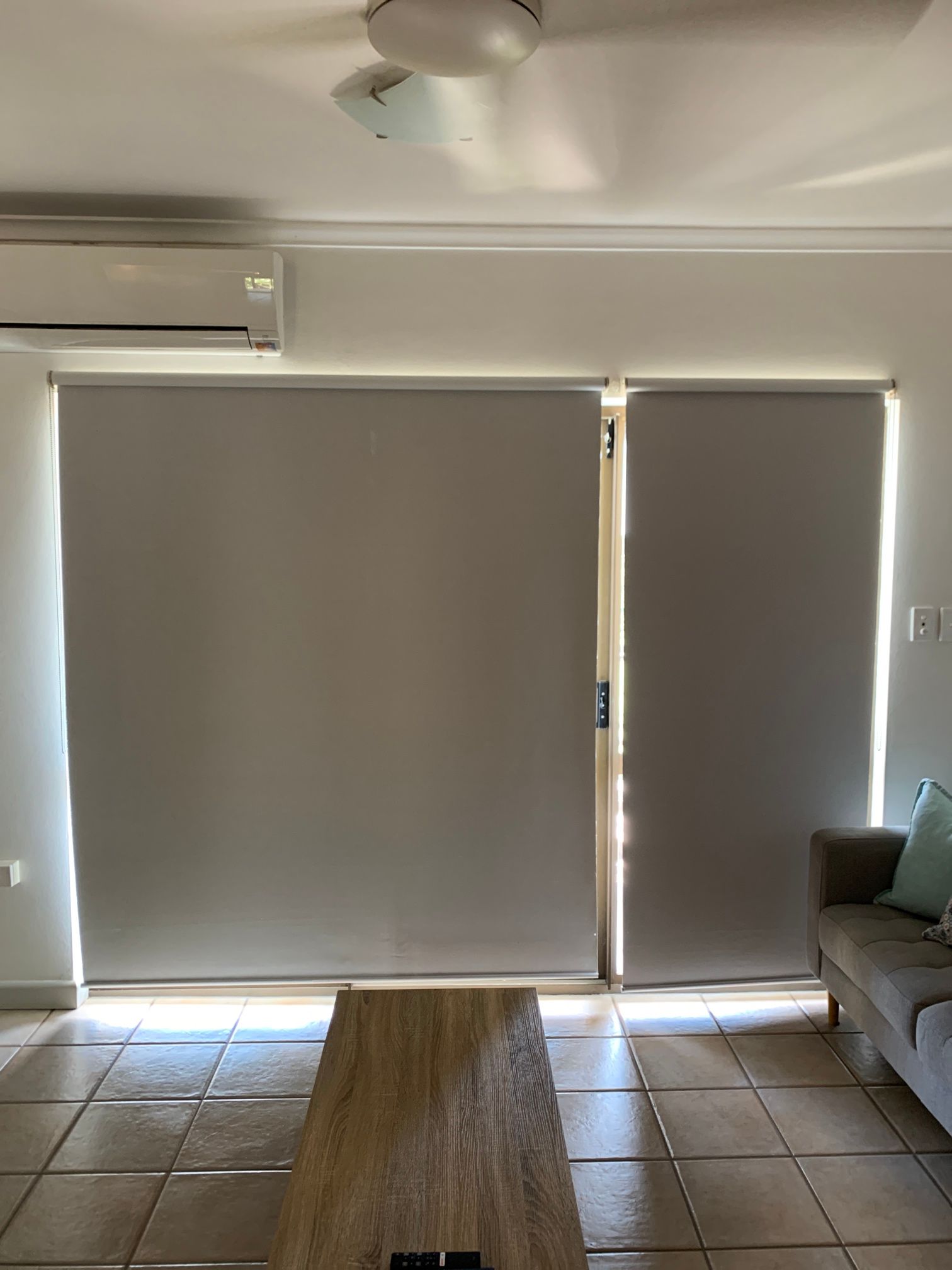 A living room with a couch , table , blinds and a ceiling fan.